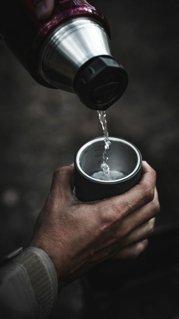 A close-up shot of water being poured from a thermos into a cup outdoors, capturing the essence of outdoor activities.