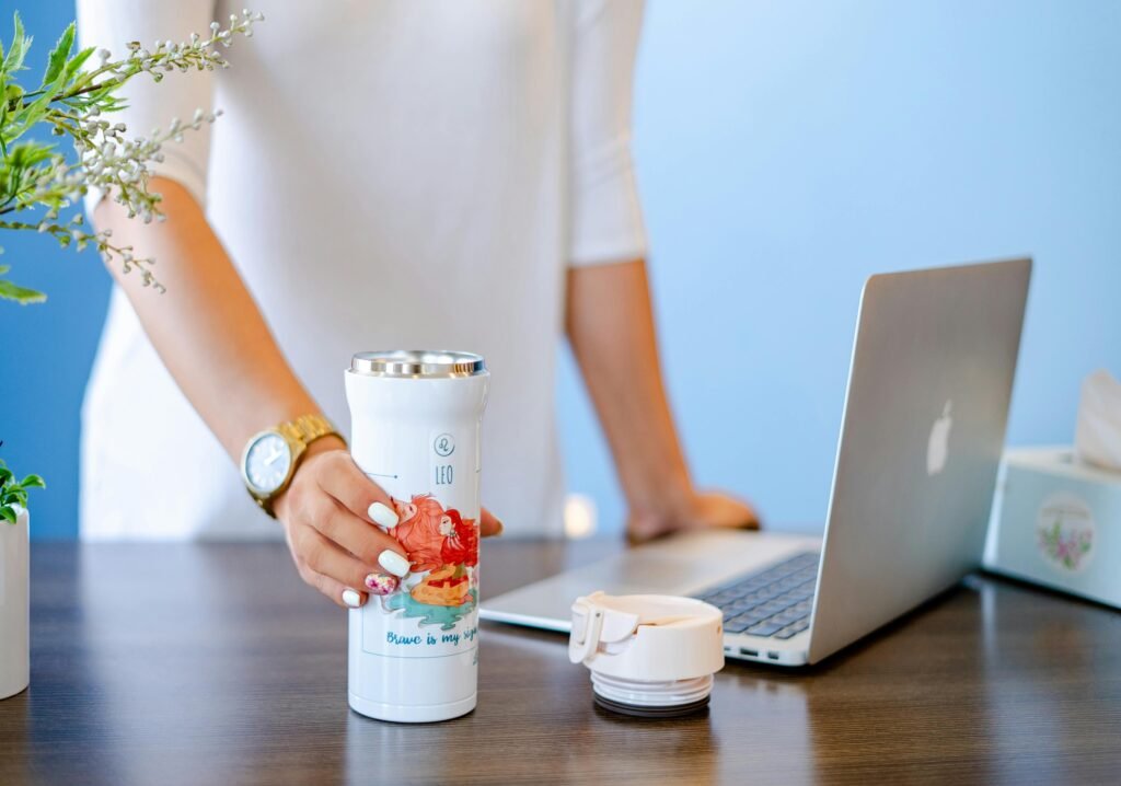 Person with a tumbler and laptop in a modern office setting, showcasing a relaxed workspace.